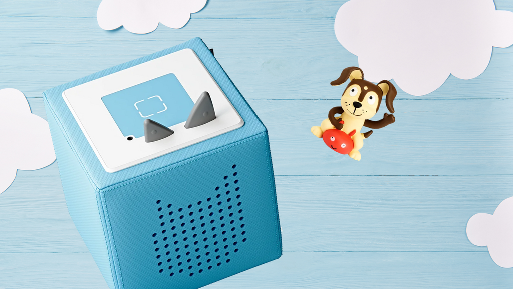 Image of a blue Tonie Box and Playful Puppy Tonie character on a wooden background with paper cut out like clouds