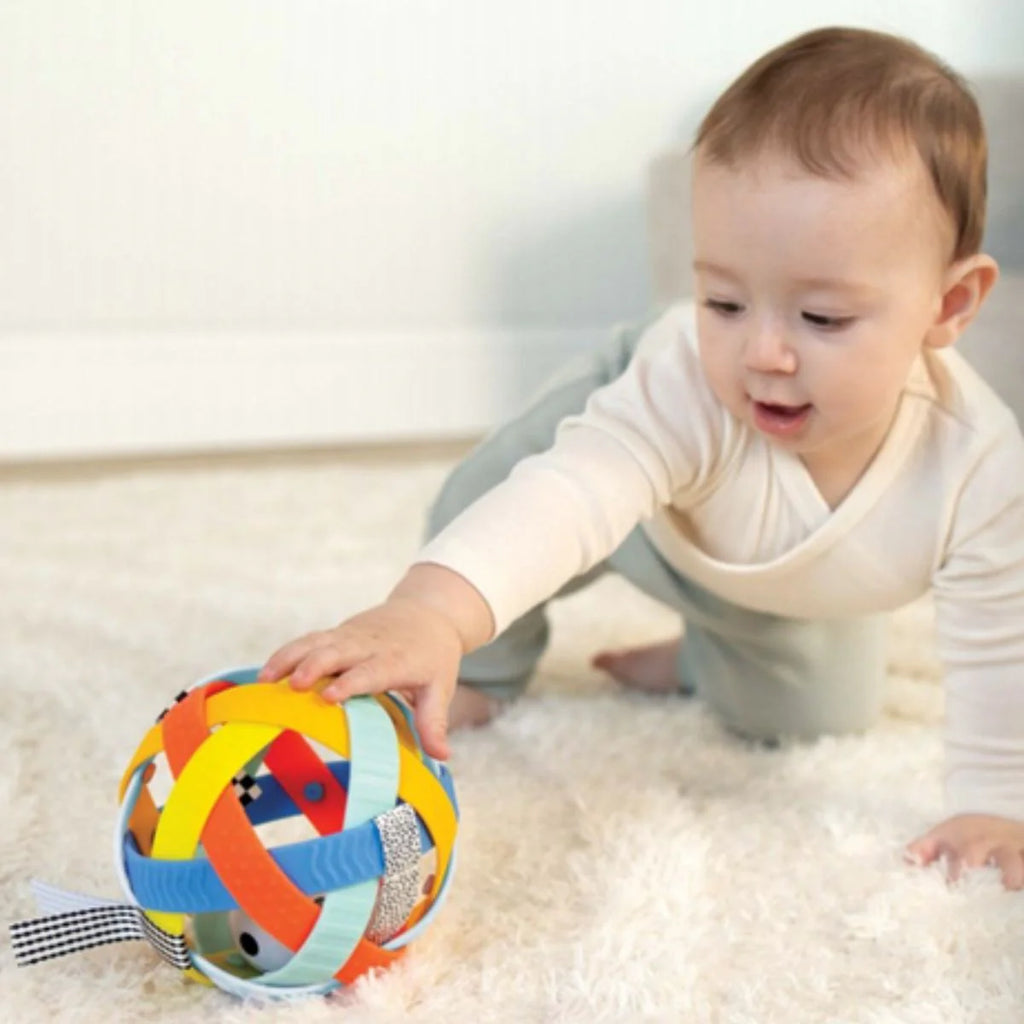 Image of a baby playing with a colorful activity ball on a white rug