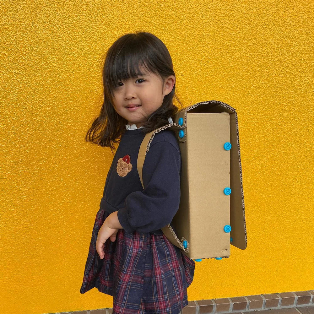 Child with a cardboard backpack against a yellow wall