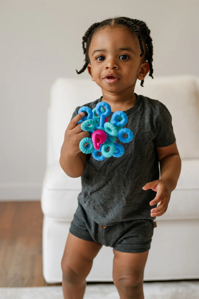 Child holding a blue and pink flower-shaped toy indoors