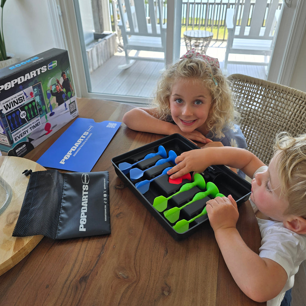 Two children playing with a darts game on a wooden table.