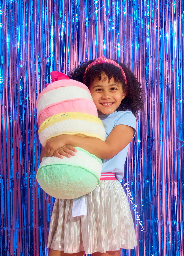 Child holding a colorful macaron-shaped pillow against a vibrant, metallic curtain background