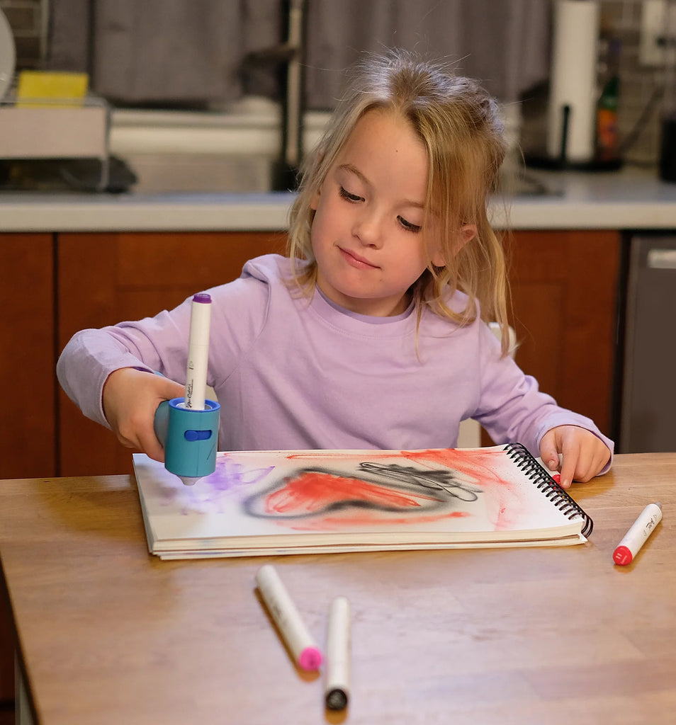 Child drawing with markers on a book at a kitchen table