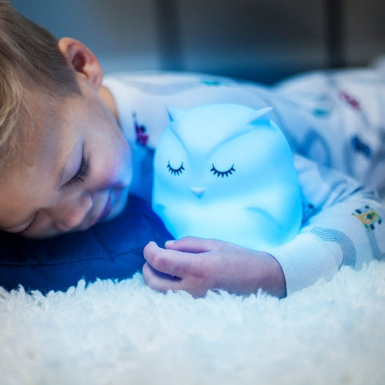 Image of child holding Owl Night Lamp Companion glowing in blue color